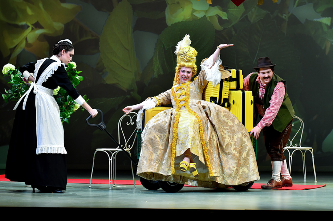 Students wearing a yellow, historical costume, singing on stage.